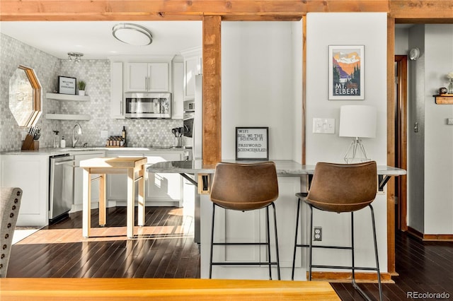 bar with sink, white cabinetry, appliances with stainless steel finishes, hardwood / wood-style flooring, and decorative backsplash