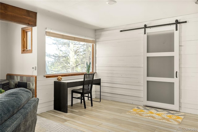 interior space with a barn door, light wood-type flooring, and wood walls