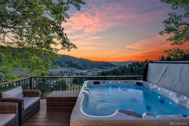 pool at dusk with an outdoor hot tub and a deck with mountain view