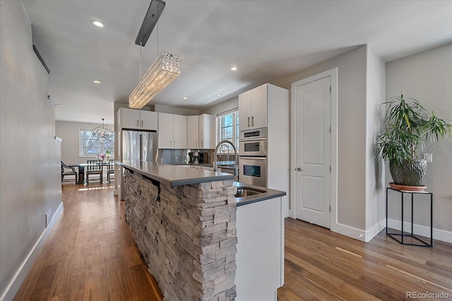 kitchen with a breakfast bar, decorative light fixtures, white cabinetry, an island with sink, and stainless steel appliances