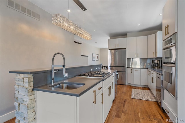 kitchen with stainless steel appliances, sink, white cabinets, and decorative light fixtures