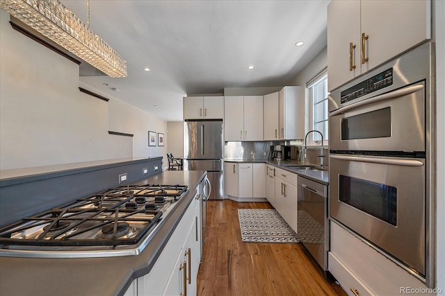 kitchen featuring sink, white cabinetry, stainless steel appliances, light hardwood / wood-style floors, and decorative light fixtures