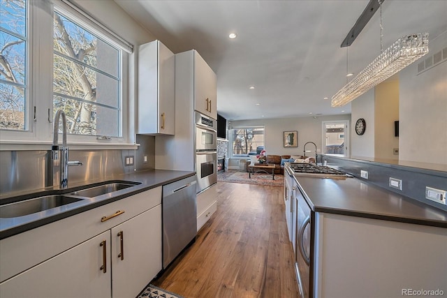 kitchen with sink, white cabinetry, decorative light fixtures, appliances with stainless steel finishes, and hardwood / wood-style floors