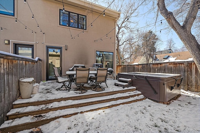 snow covered rear of property with a hot tub