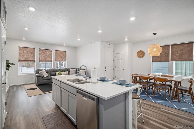 kitchen with stainless steel dishwasher, sink, pendant lighting, gray cabinets, and an island with sink