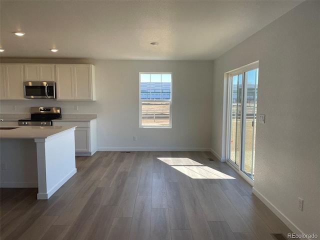 kitchen with baseboards, wood finished floors, stainless steel appliances, light countertops, and white cabinetry