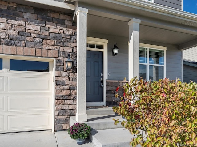 doorway to property with an attached garage, stone siding, and a porch