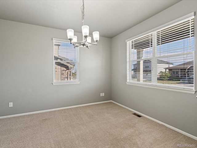 spare room with a chandelier, carpet floors, visible vents, and baseboards