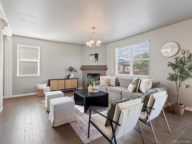 living room featuring a fireplace, an inviting chandelier, a textured ceiling, baseboards, and hardwood / wood-style flooring