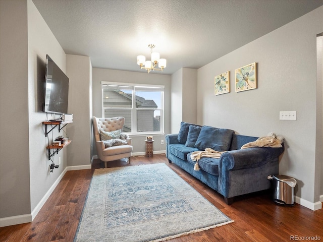 living area with baseboards, a textured ceiling, wood finished floors, and a notable chandelier