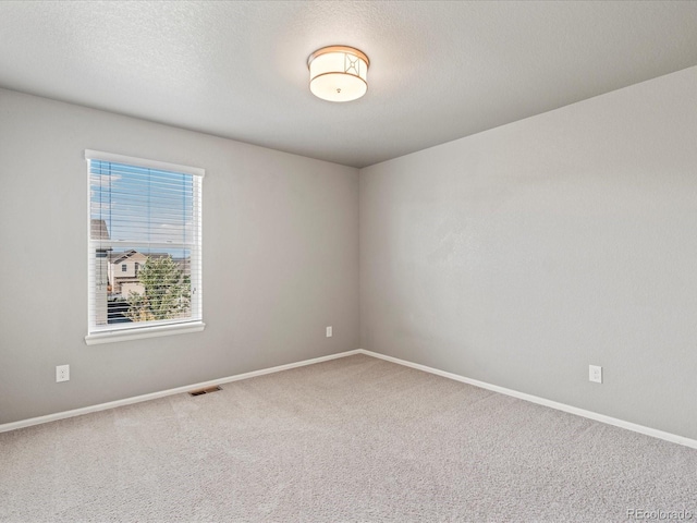 empty room with carpet, visible vents, a textured ceiling, and baseboards