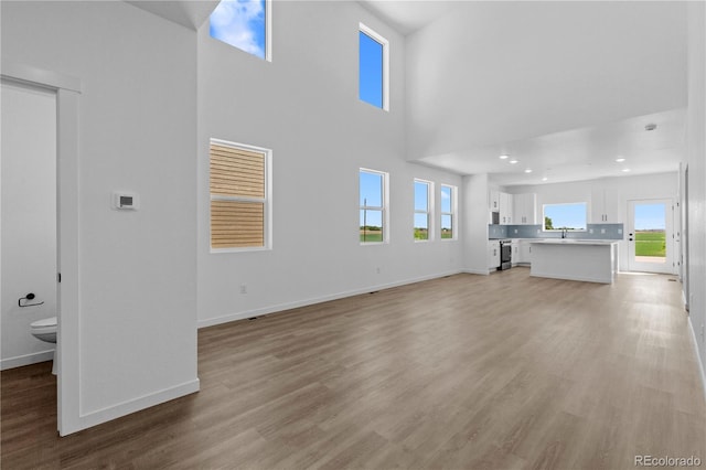 unfurnished living room featuring light wood finished floors, baseboards, a towering ceiling, and a sink