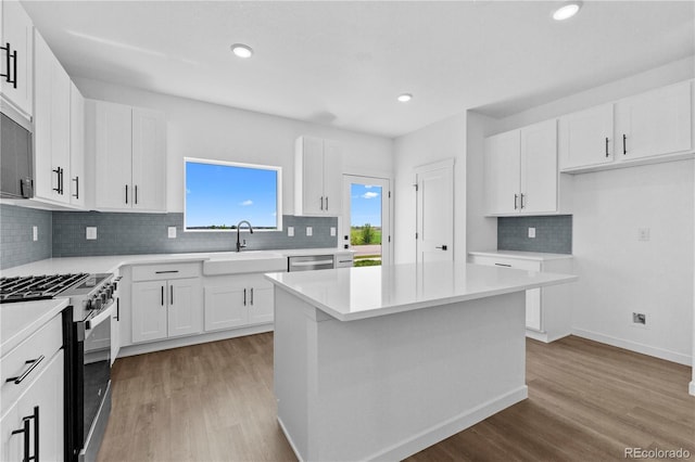 kitchen featuring appliances with stainless steel finishes, a sink, light wood-style flooring, backsplash, and white cabinetry