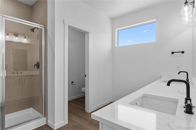 full bathroom featuring a stall shower, toilet, wood finished floors, baseboards, and double vanity