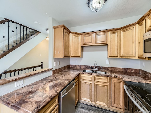 kitchen featuring dark stone countertops, appliances with stainless steel finishes, a peninsula, wood finished floors, and a sink