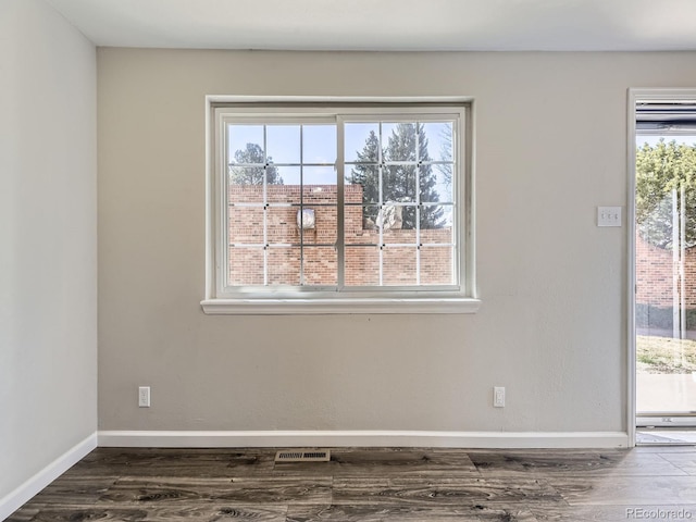 unfurnished room featuring dark wood-style floors, visible vents, a healthy amount of sunlight, and baseboards