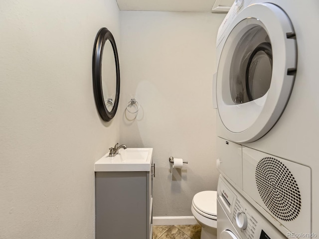 half bathroom with toilet, stacked washer and clothes dryer, vanity, and baseboards