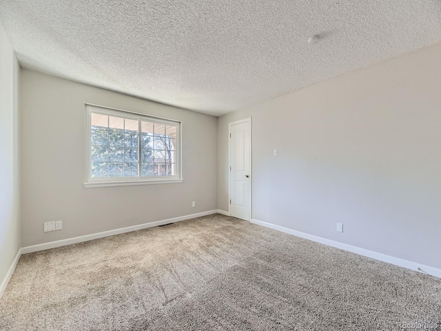 carpeted spare room with a textured ceiling and baseboards