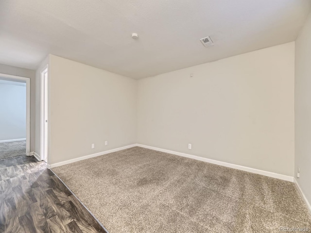 empty room featuring dark wood finished floors, visible vents, dark carpet, and baseboards