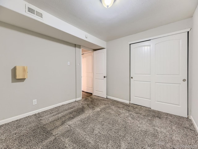 unfurnished bedroom with visible vents, a textured ceiling, a closet, carpet floors, and baseboards