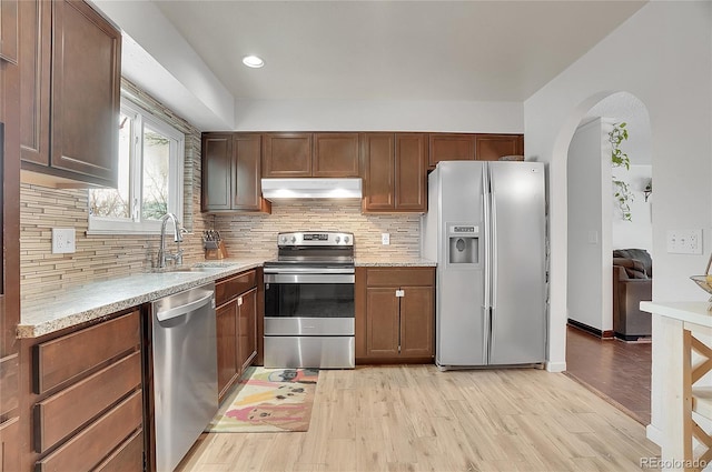 kitchen featuring arched walkways, light wood finished floors, appliances with stainless steel finishes, a sink, and under cabinet range hood