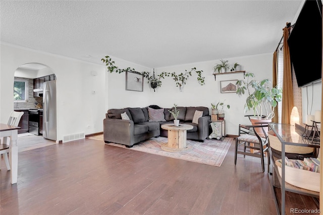 living room with baseboards, visible vents, arched walkways, wood finished floors, and a textured ceiling