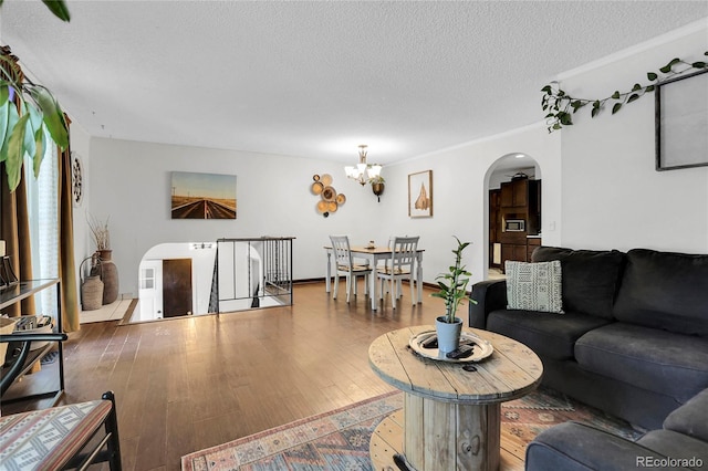 living area featuring arched walkways, a textured ceiling, an inviting chandelier, and wood finished floors