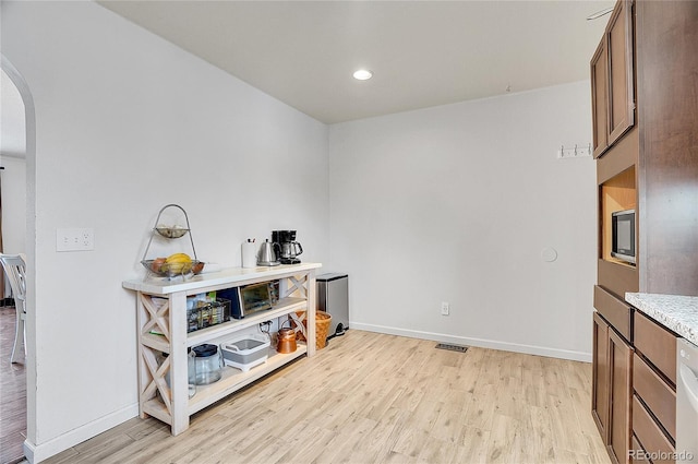 interior space featuring light wood finished floors, baseboards, visible vents, and arched walkways