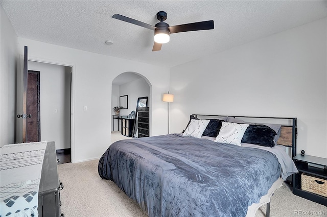 bedroom with arched walkways, ceiling fan, a textured ceiling, and light colored carpet