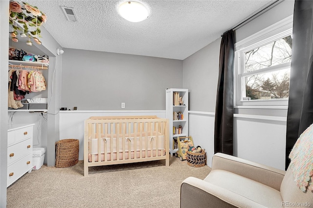 carpeted bedroom featuring a crib, visible vents, and a textured ceiling