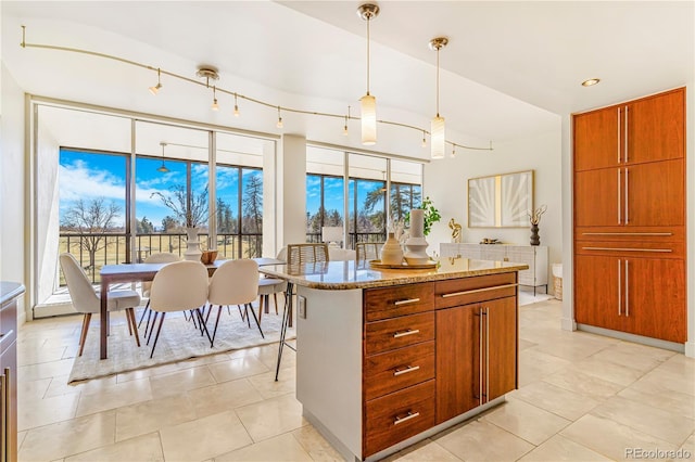 kitchen featuring brown cabinets, decorative light fixtures, a kitchen island, light tile patterned flooring, and light stone countertops