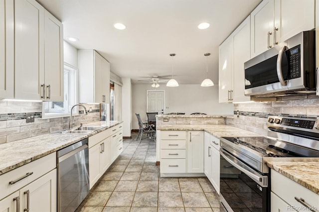 kitchen featuring sink, hanging light fixtures, stainless steel appliances, light stone countertops, and white cabinets