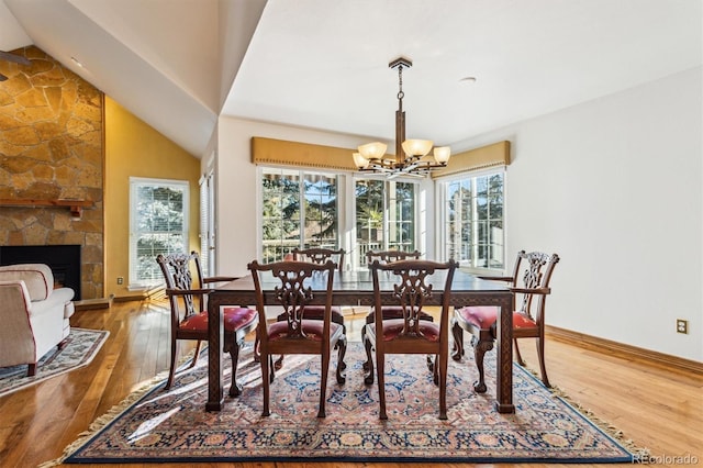 dining area with a notable chandelier, wood-type flooring, a stone fireplace, and a wealth of natural light