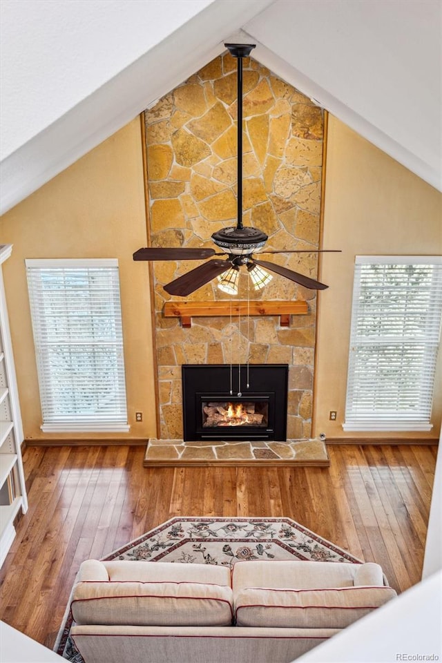 living room with wood-type flooring, a stone fireplace, ceiling fan, and high vaulted ceiling