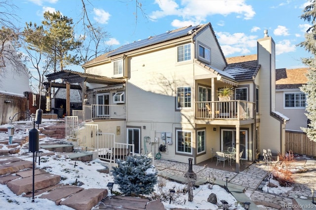 snow covered house featuring solar panels, a balcony, a patio area, and a pergola