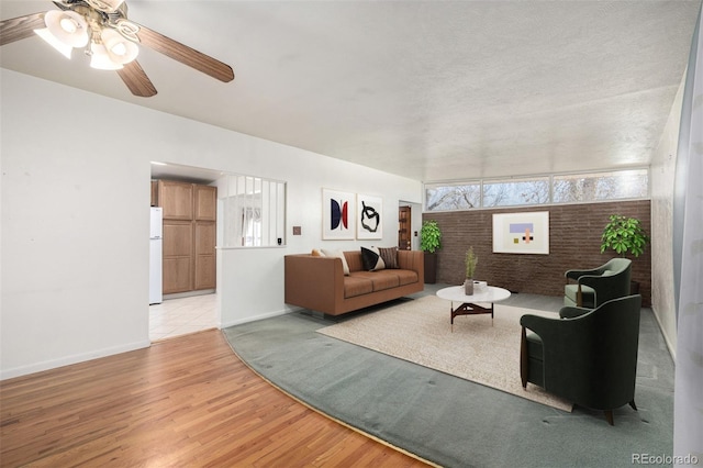 living room featuring light hardwood / wood-style floors, ceiling fan, and brick wall