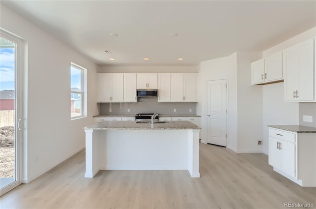 kitchen featuring light wood-type flooring, a sink, stainless steel microwave, backsplash, and white cabinetry