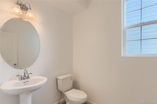 bathroom featuring toilet, baseboards, a wealth of natural light, and a sink