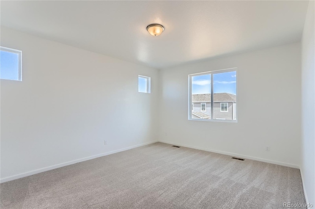 empty room with light colored carpet, visible vents, and baseboards