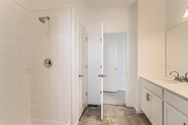 full bath featuring tiled shower, vanity, and baseboards