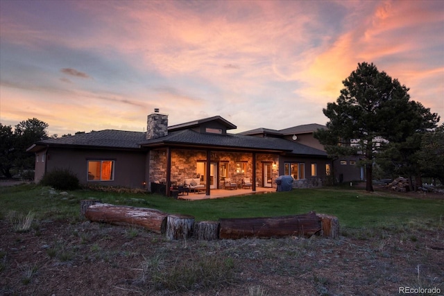 17158 County Road 363, Buena Vista, CO 81211 - back of house at dusk featuring a chimney, a patio area, stone siding, a yard, and an outdoor living space