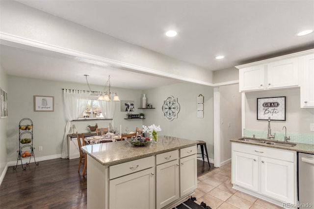 kitchen with light stone counters, a kitchen island, a sink, white cabinets, and dishwasher