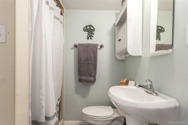 bathroom featuring a shower with shower curtain, toilet, and a sink