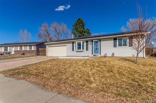 ranch-style house with a front lawn, roof mounted solar panels, fence, concrete driveway, and a garage