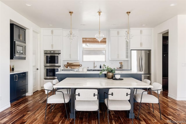 kitchen featuring white cabinets, a kitchen island, light stone counters, stainless steel appliances, and pendant lighting