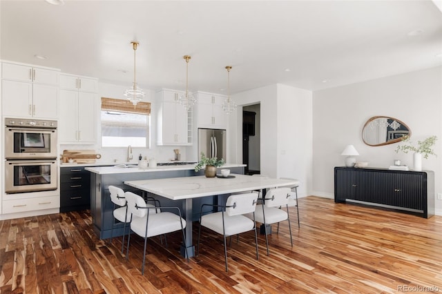 kitchen with a center island, stainless steel appliances, hanging light fixtures, white cabinets, and a kitchen breakfast bar