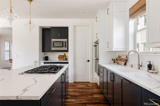 kitchen featuring white cabinets, appliances with stainless steel finishes, light stone counters, hanging light fixtures, and a sink