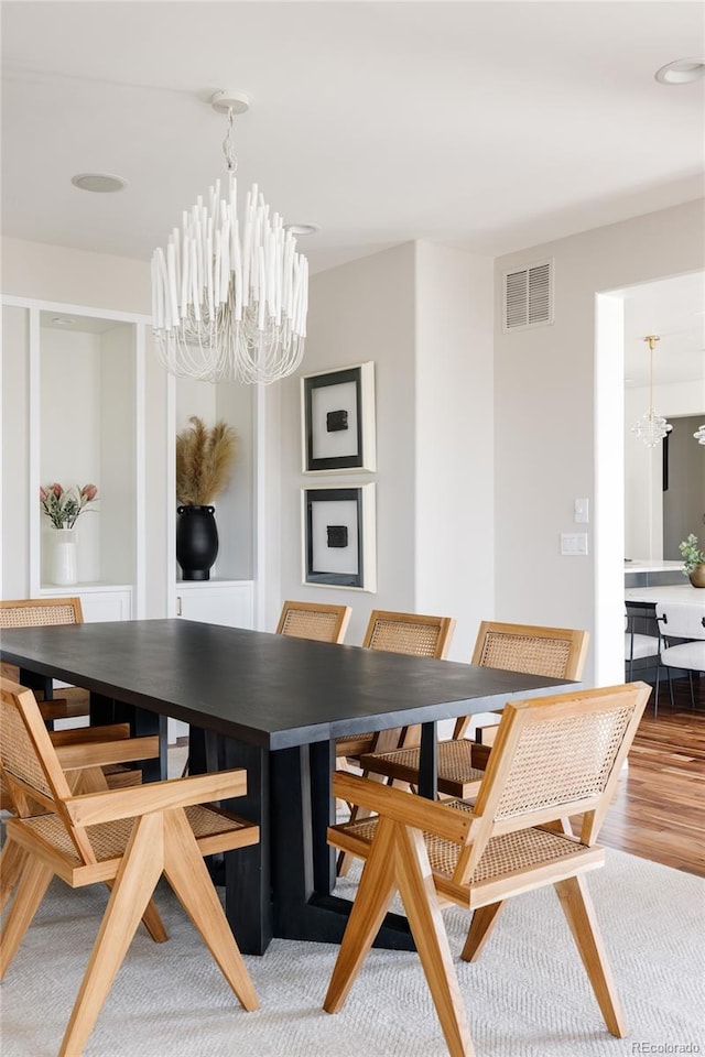 dining room featuring wood finished floors, visible vents, and an inviting chandelier