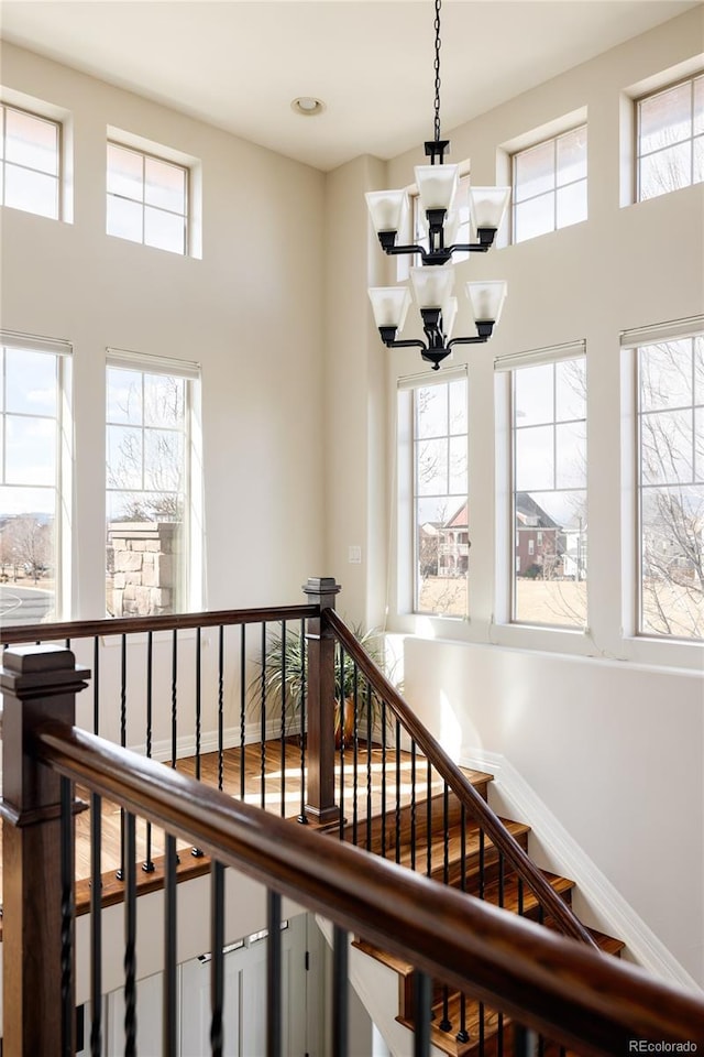 stairs with baseboards, wood finished floors, a towering ceiling, and an inviting chandelier