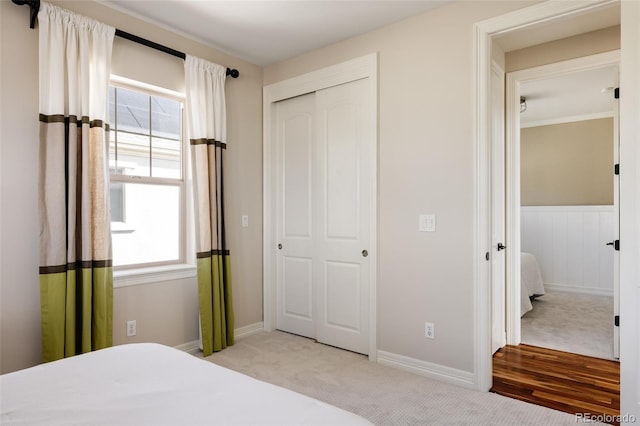 bedroom featuring a closet, light colored carpet, and wainscoting